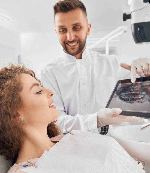 Male doctor showing x-ray pictures of teeth on tablet Handsome male doctor in white medical uniform and rubber gloves holding electronic tablet and showing beautiful female client x-ray pictures of her teeth. Concept of dentistry.